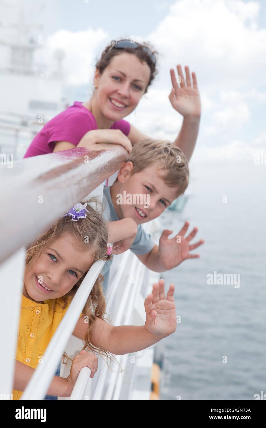 Mère avec ses enfants debout sur le pont d'un grand navire à passagers près des mains courantes et agitant leurs mains, concentrez-vous sur la fille Banque D'Images