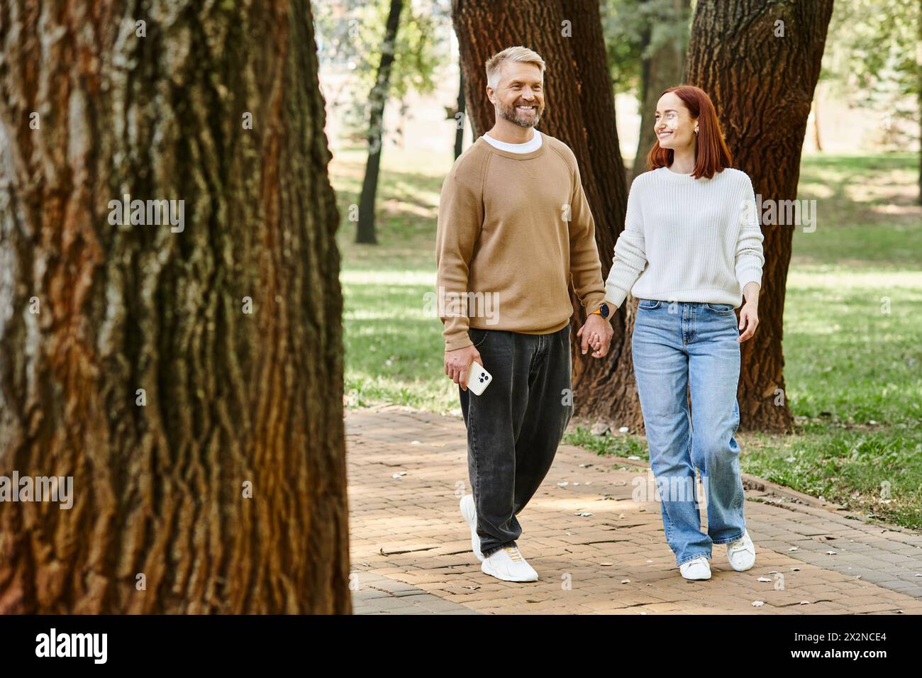 Un homme et une femme en tenue décontractée marchent ensemble dans un cadre paisible de parc. Banque D'Images