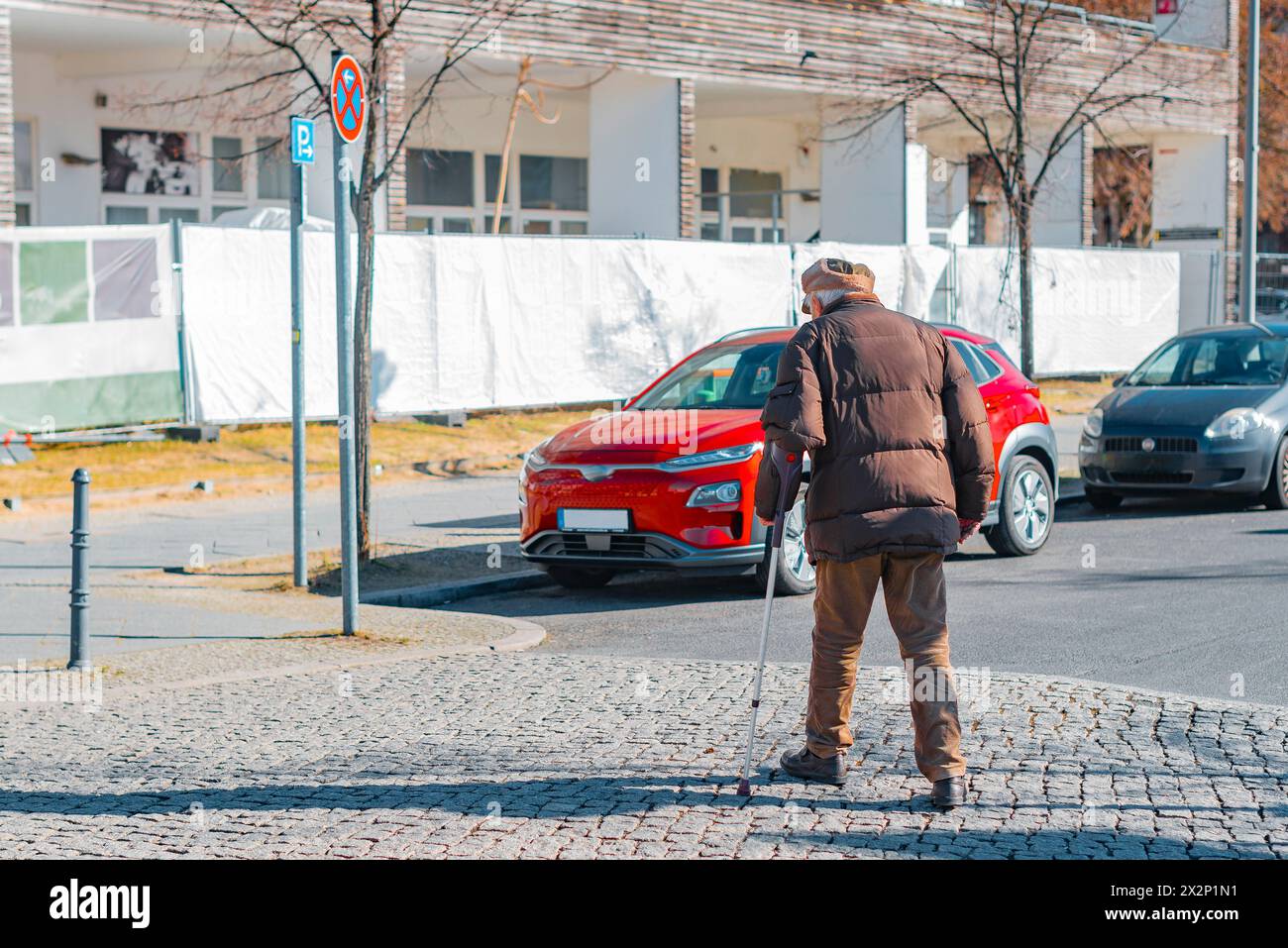 Un vieil homme avec un bâton de marche traverse une rue, photographié par derrière Banque D'Images