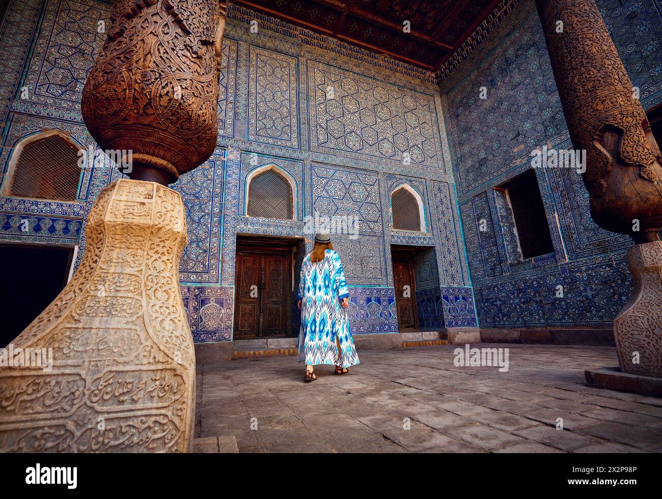 Femme touriste en robe ethnique à la cour intérieure de la salle de palais en mosaïque bleue à Tash Hauli avec colonne en bois à l'ancienne ville Khiva en Ouzbékistan. Banque D'Images