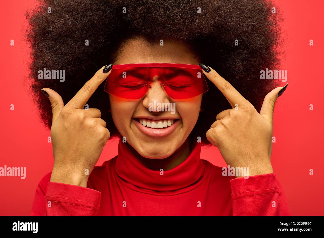 Femme afro-américaine élégante avec des eyeliners rouges et bandeau sur fond vibrant. Banque D'Images