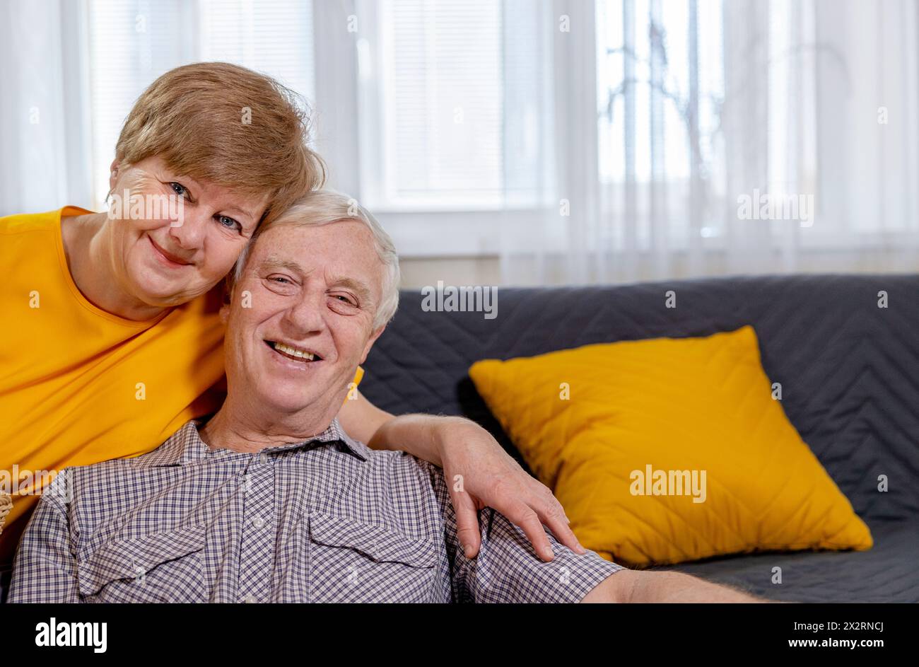 Couple senior souriant assis à la maison Banque D'Images
