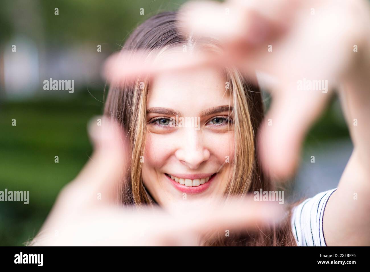 Jeune femme souriante regardant à travers le cadre du doigt Banque D'Images
