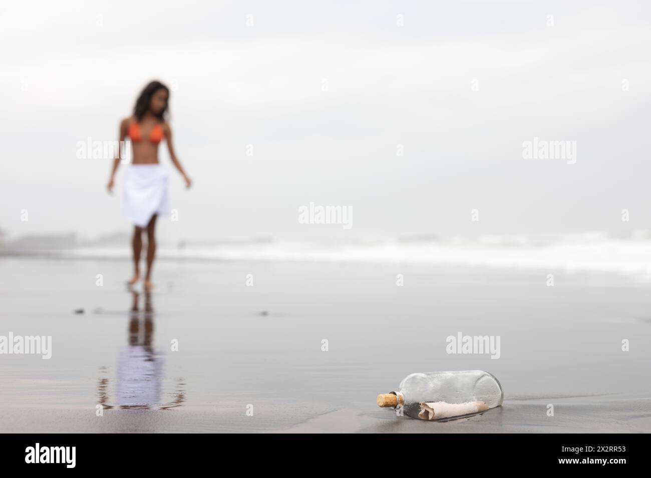 Message dans une bouteille en verre avec femme sur le sable humide à la plage Banque D'Images