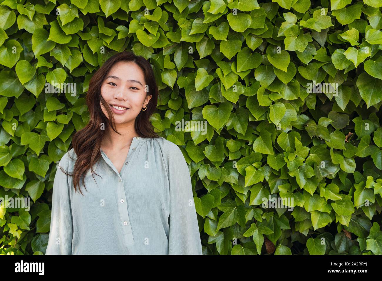 Femme souriante debout devant une haie verte Banque D'Images