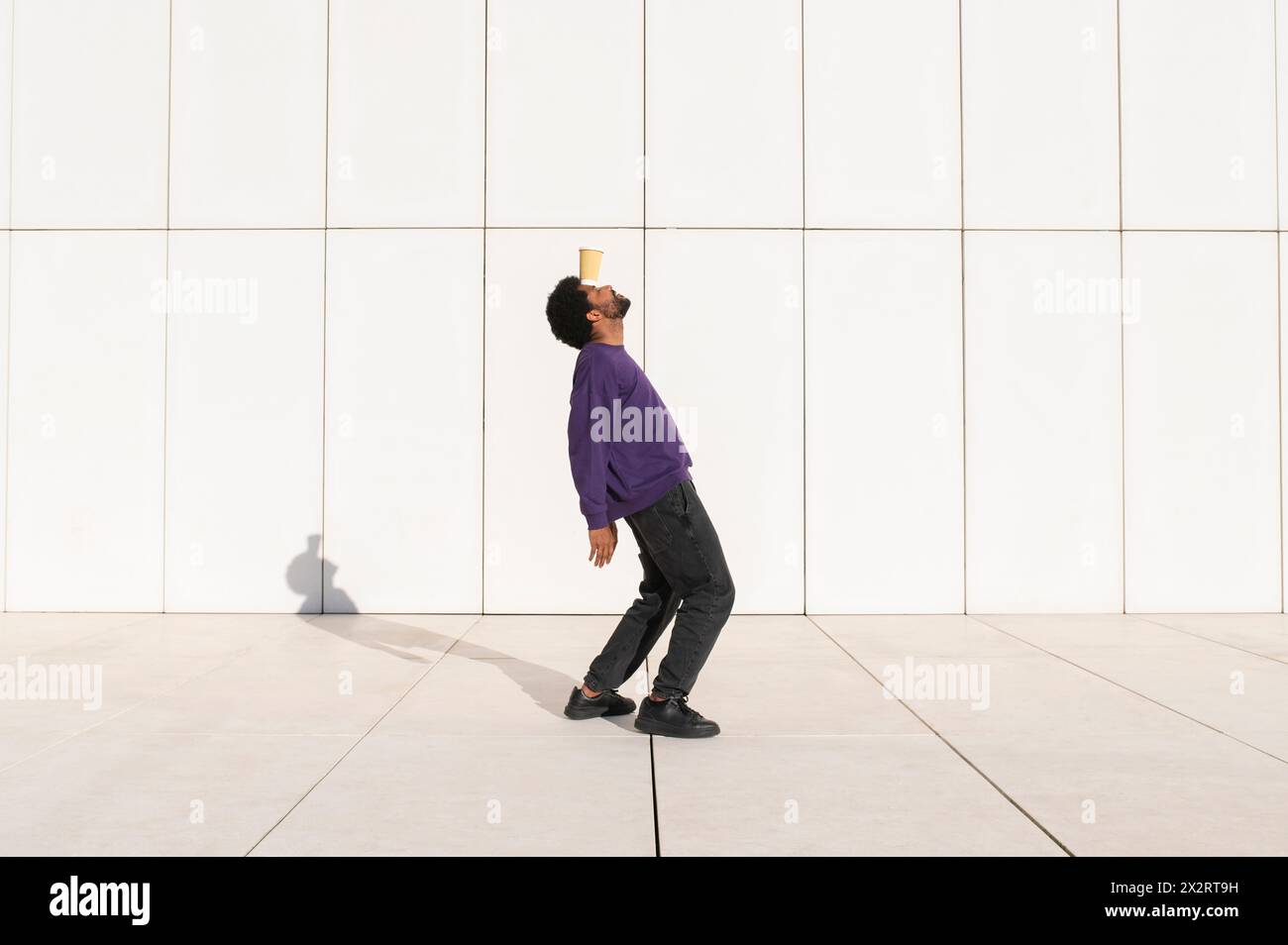 Jeune homme équilibrant tasse sur le front devant le mur blanc Banque D'Images
