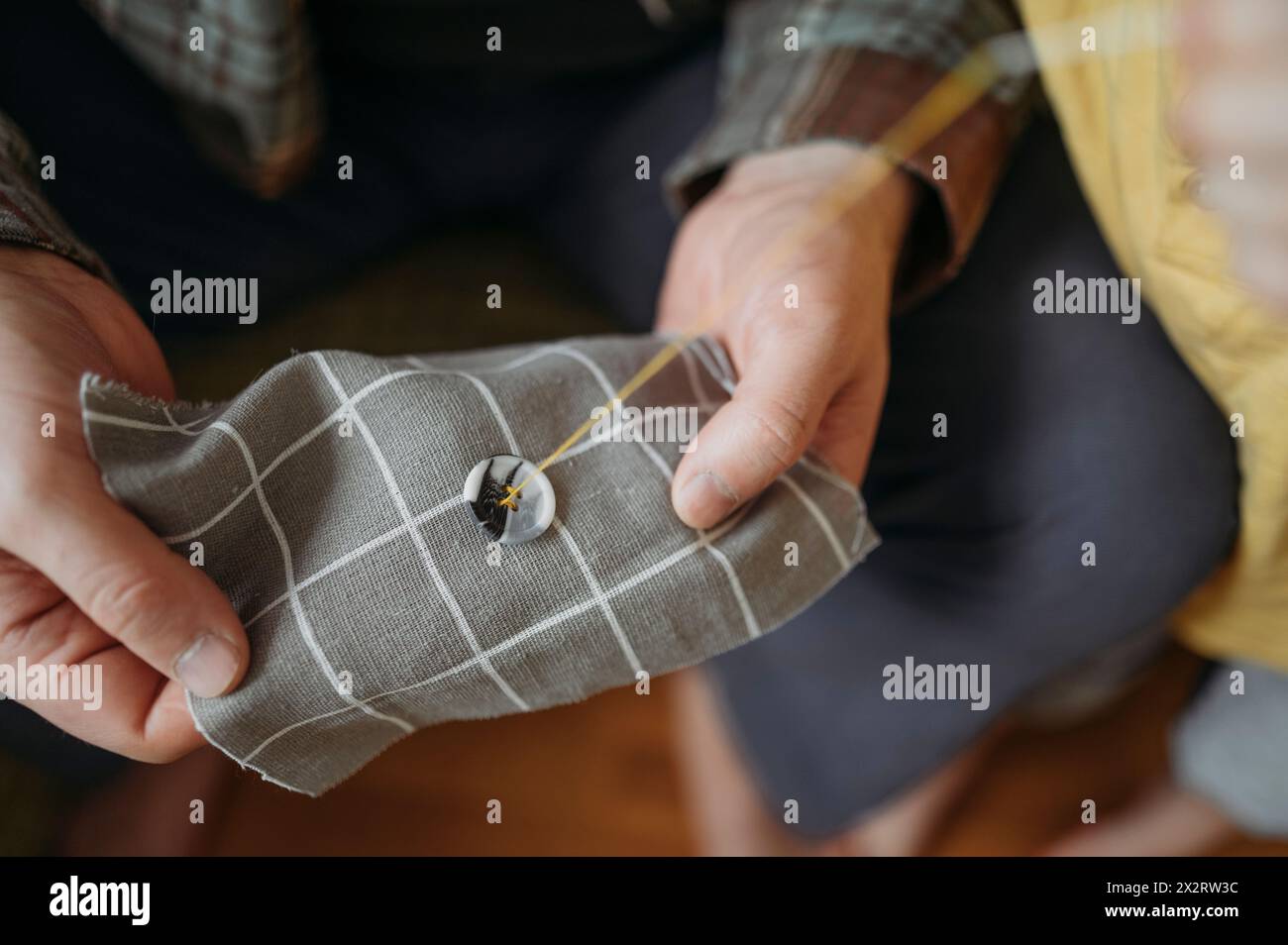 Homme coudre bouton sur tissu de couleur grise Banque D'Images