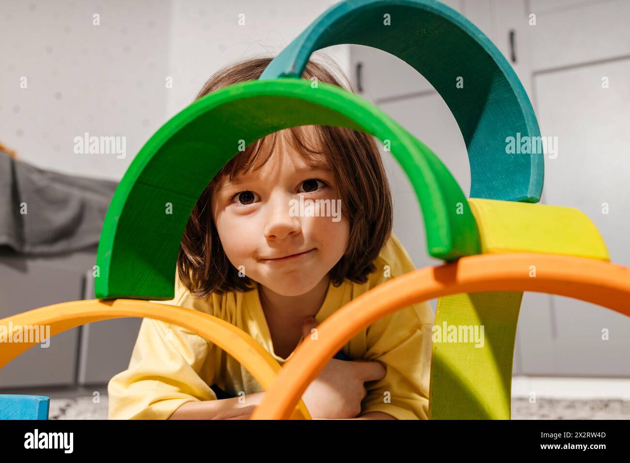 Garçon souriant jouant avec un jouet pyramidal en forme d'arc-en-ciel à la maison Banque D'Images