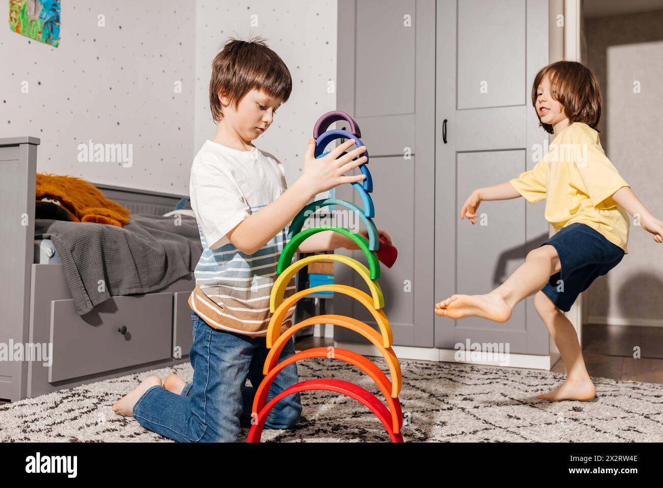 Garçon heureux avec frère construisant pyramide avec des jouets arc-en-ciel colorés à la maison Banque D'Images