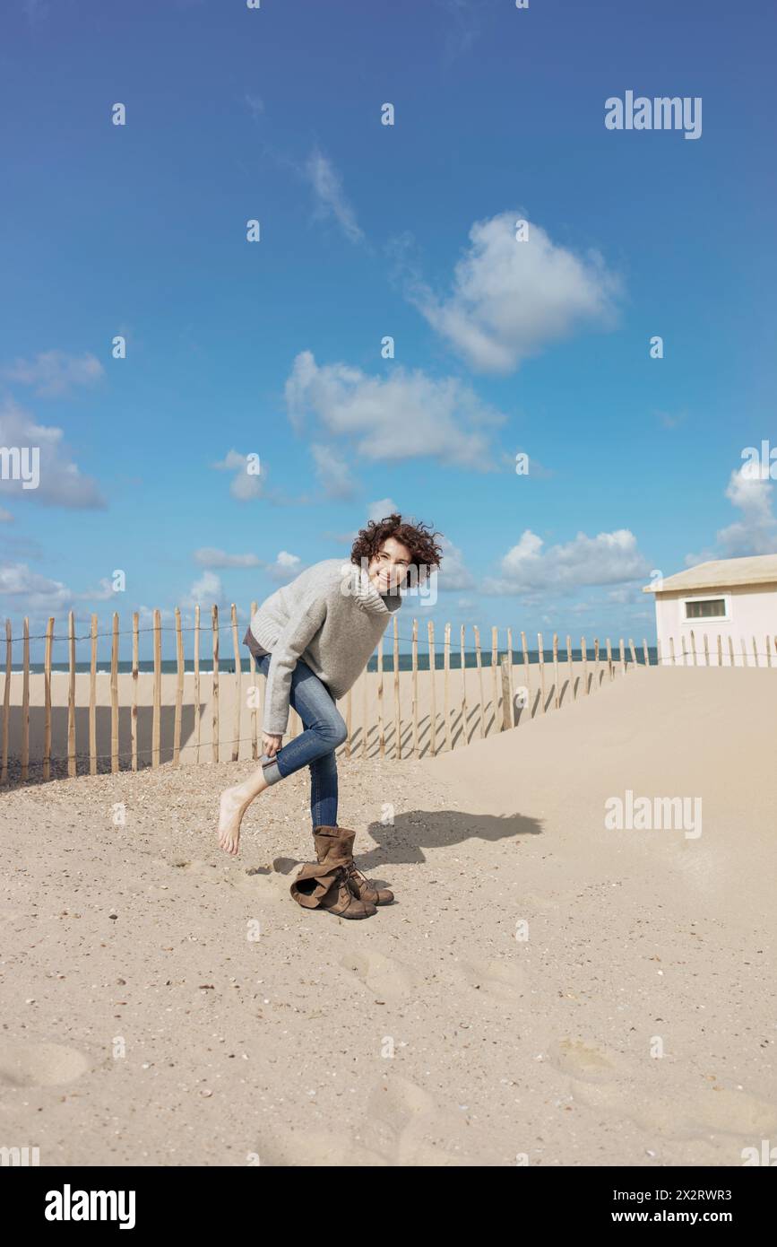 Femme heureuse portant des chaussures à la plage le jour ensoleillé Banque D'Images