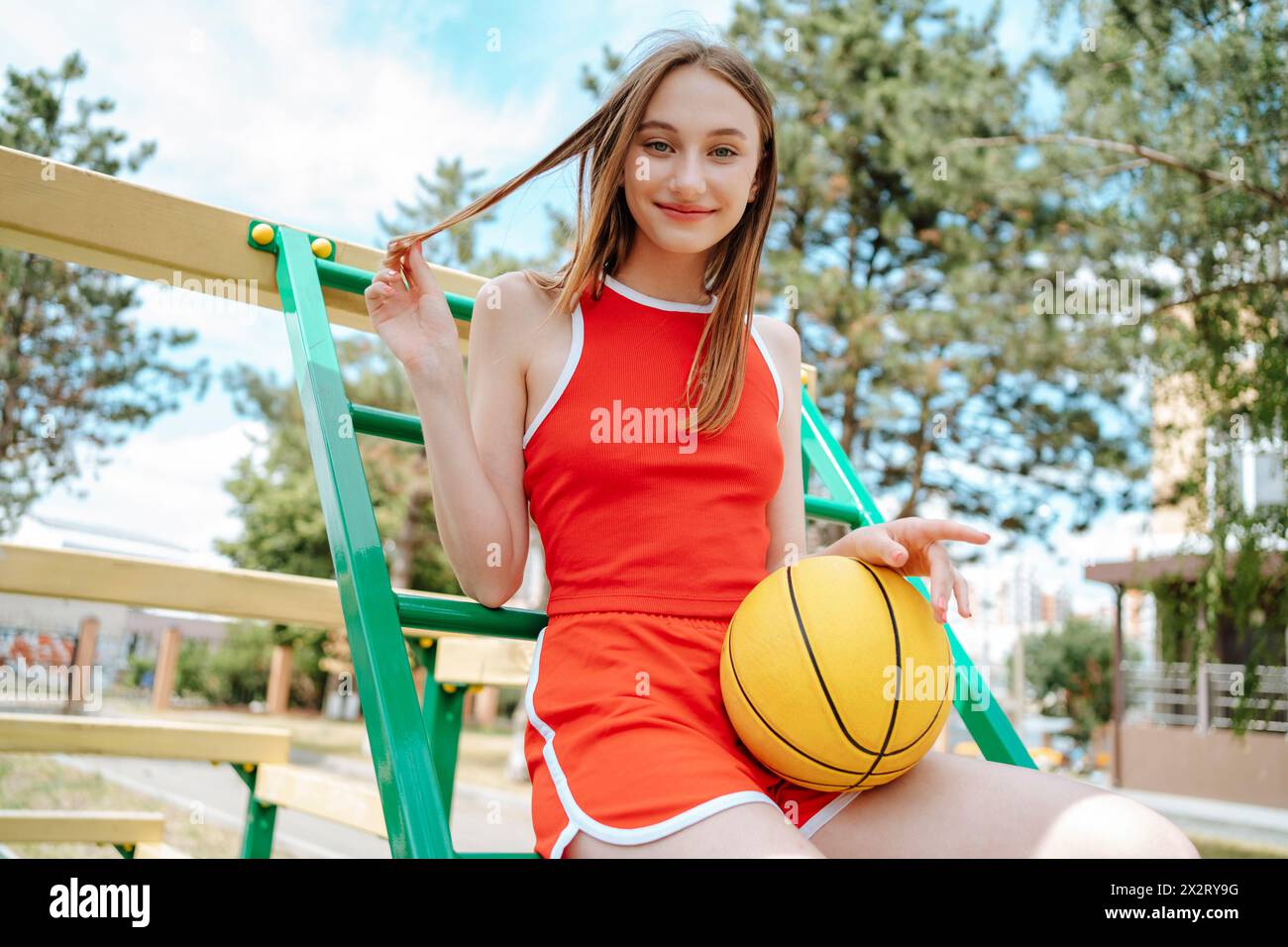 Joueur de basket-ball souriant assis avec la balle sur les marches dans le terrain de jeu Banque D'Images
