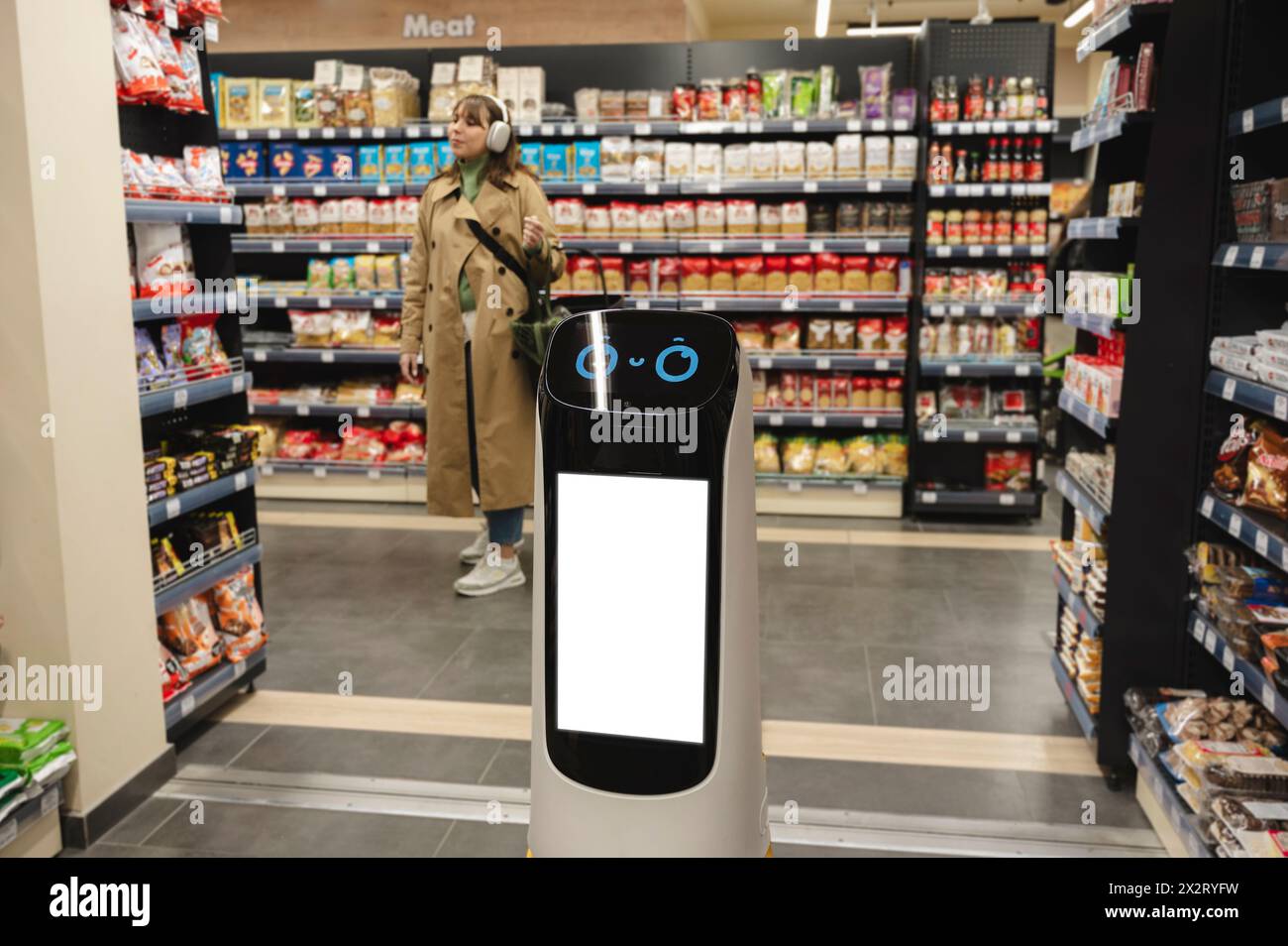 Robot de livraison intelligent près des étagères d'épicerie avec femme en arrière-plan au supermarché Banque D'Images