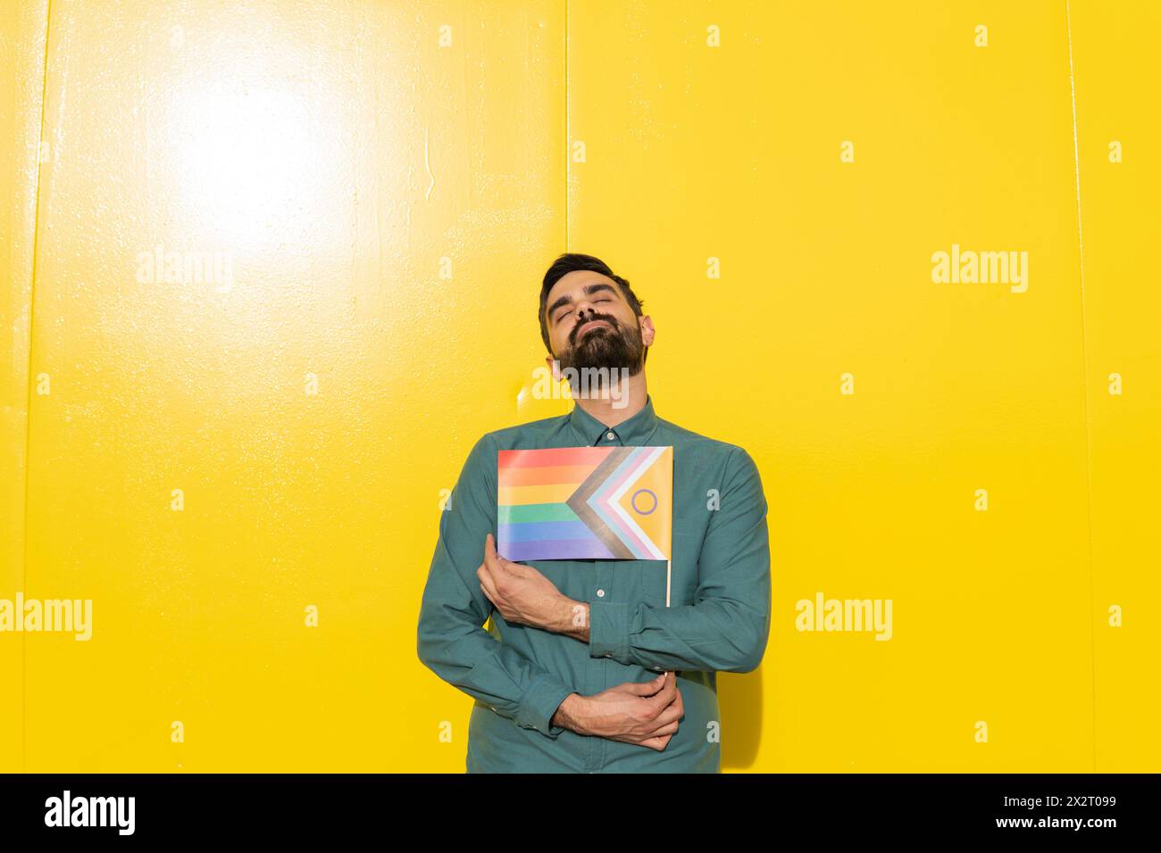 Homme tenant le drapeau arc-en-ciel et appuyé sur le mur jaune Banque D'Images