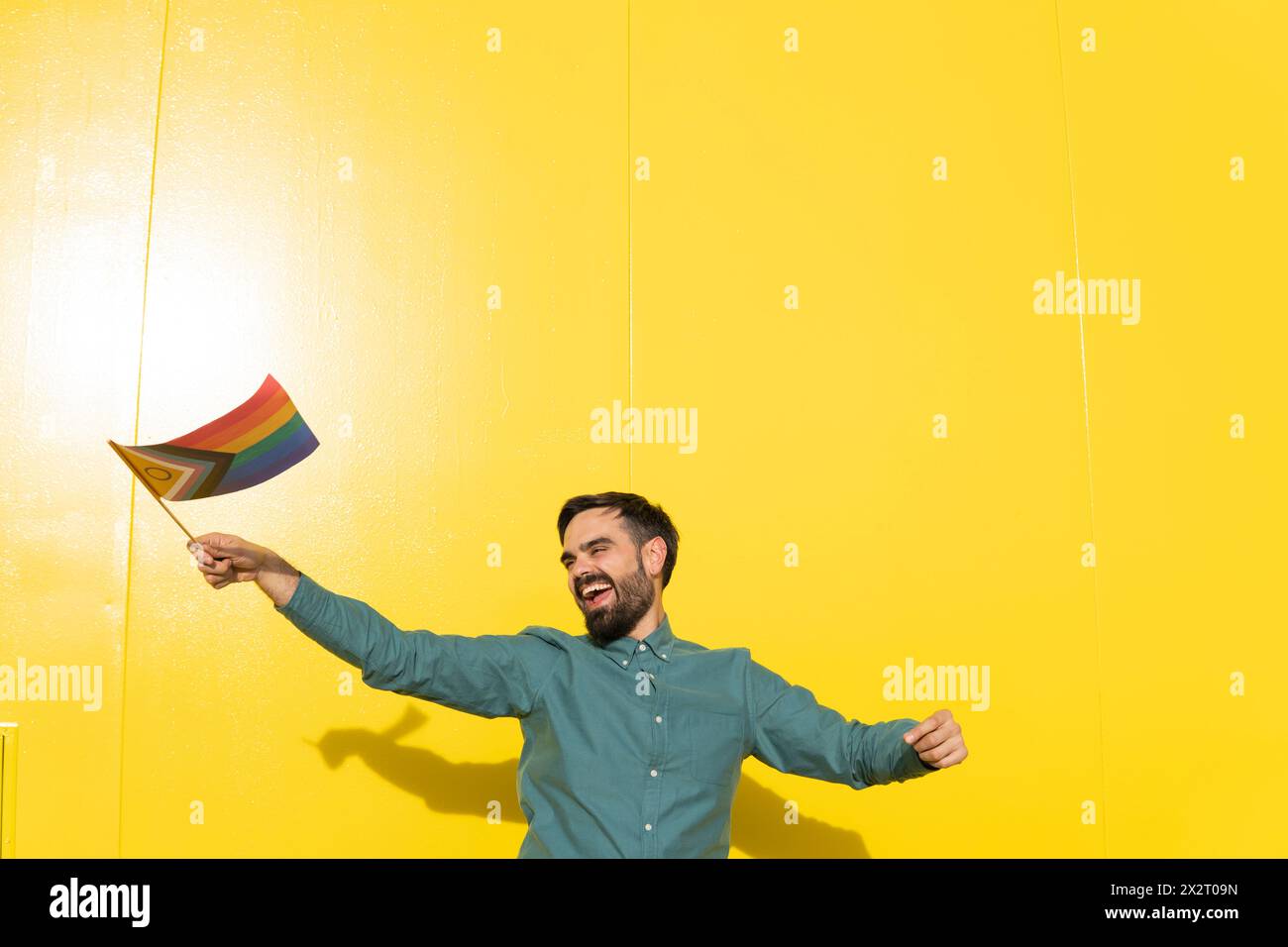 Homme heureux tenant le drapeau de la fierté LGBTIQ devant le mur jaune Banque D'Images