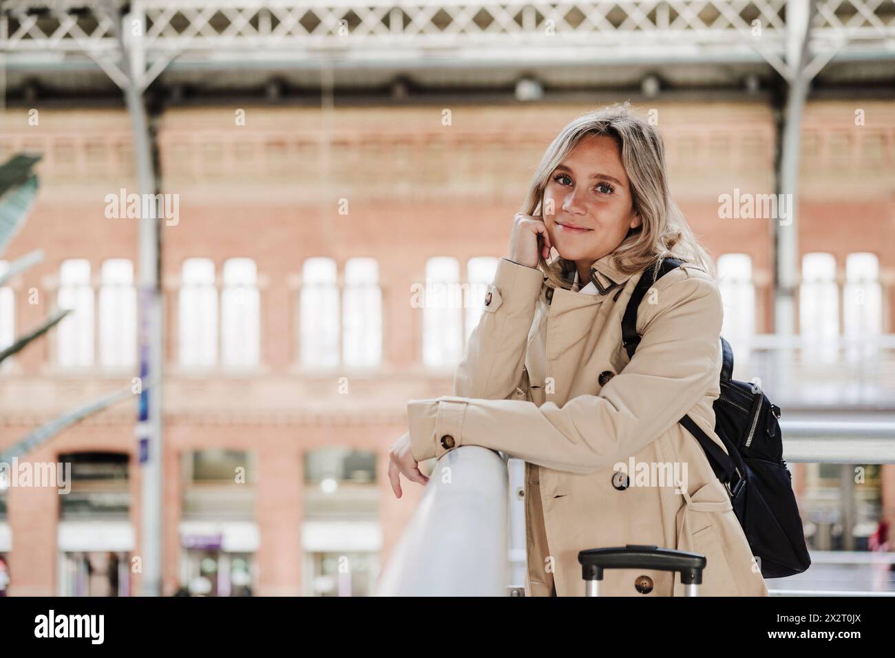 Femme souriante appuyée sur le coude près de la rambarde à la gare Banque D'Images