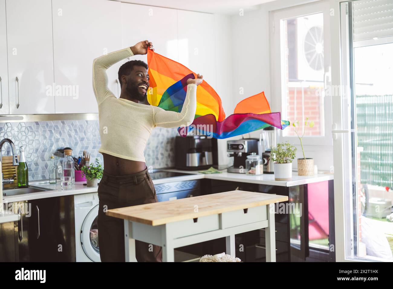 Personne heureuse non binaire jouant avec le drapeau arc-en-ciel à la maison Banque D'Images