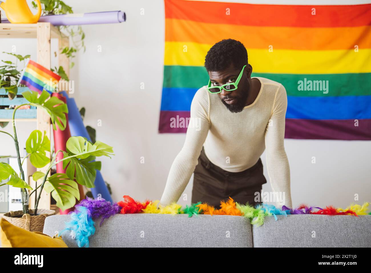 Personne non binaire à la mode portant des lunettes de soleil et s'appuyant sur un canapé à la maison Banque D'Images