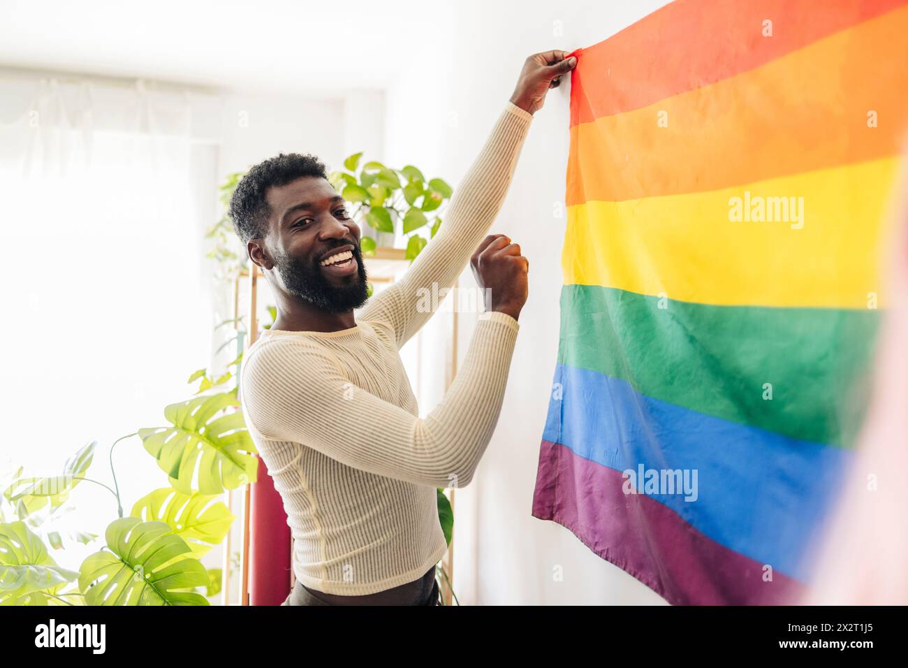 Personne heureuse non binaire collant le drapeau arc-en-ciel sur le mur à la maison Banque D'Images
