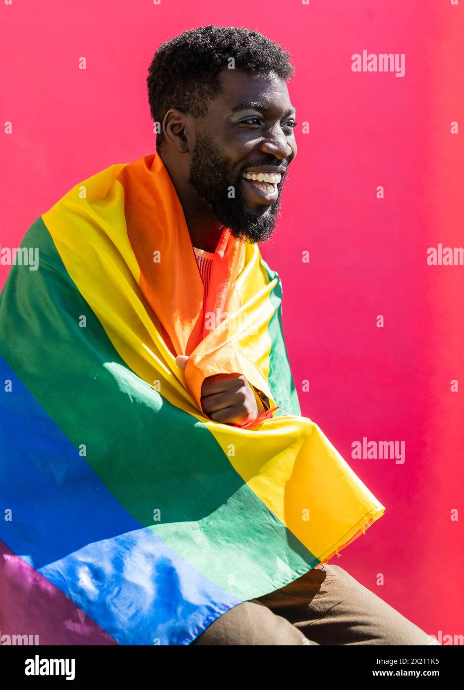 Personne non binaire heureuse couverte d'un drapeau coloré sur fond rose Banque D'Images