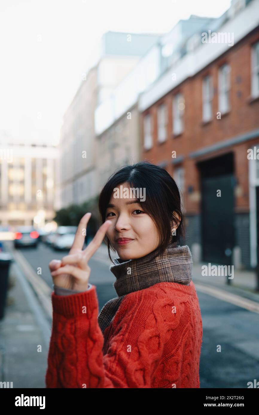Jeune femme gestuelle signe de paix dans la rue Banque D'Images
