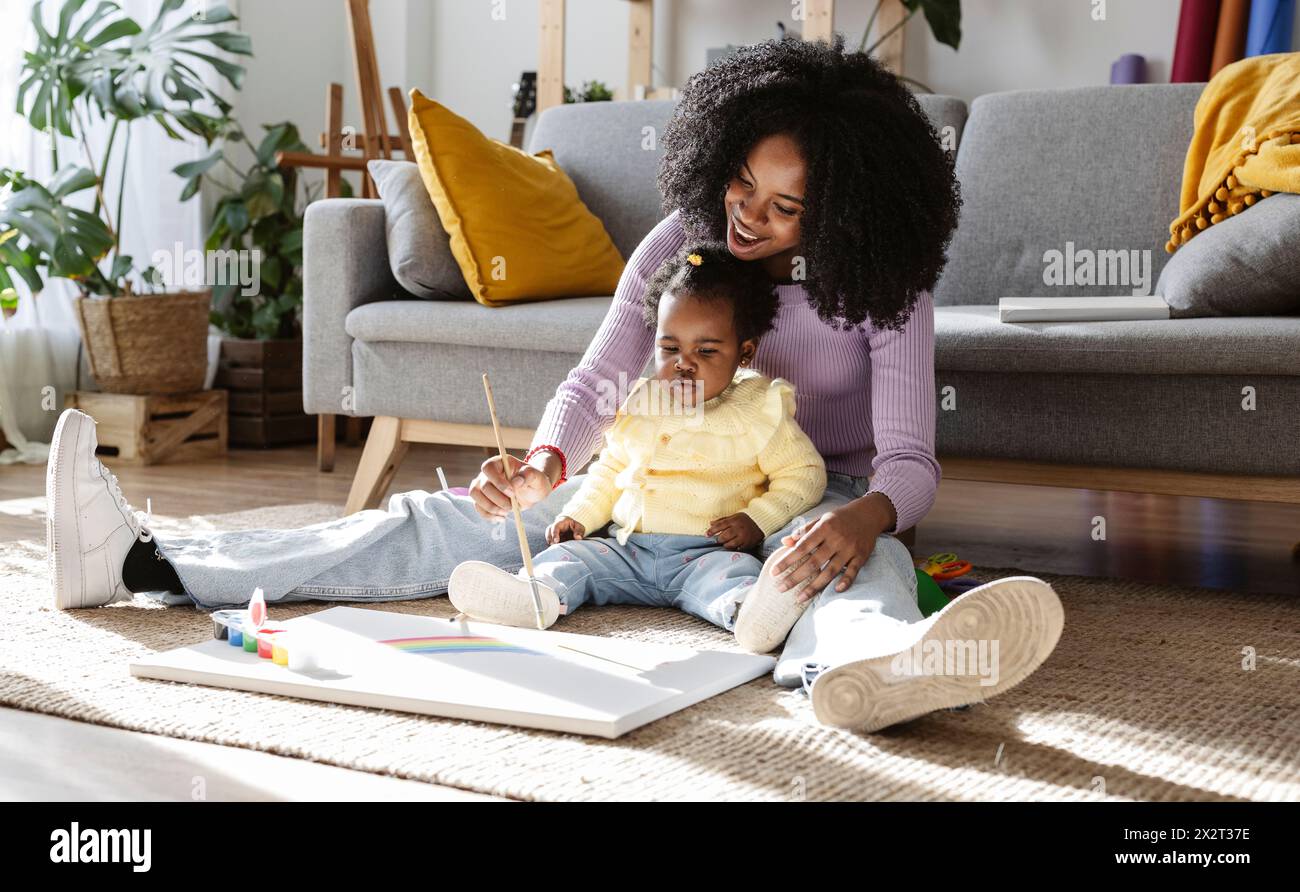 Heureuse mère peignant arc-en-ciel assis avec sa fille sur la moquette dans le salon Banque D'Images