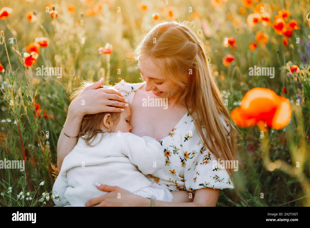 Mère souriante allaitant fille dans le champ de fleurs Banque D'Images