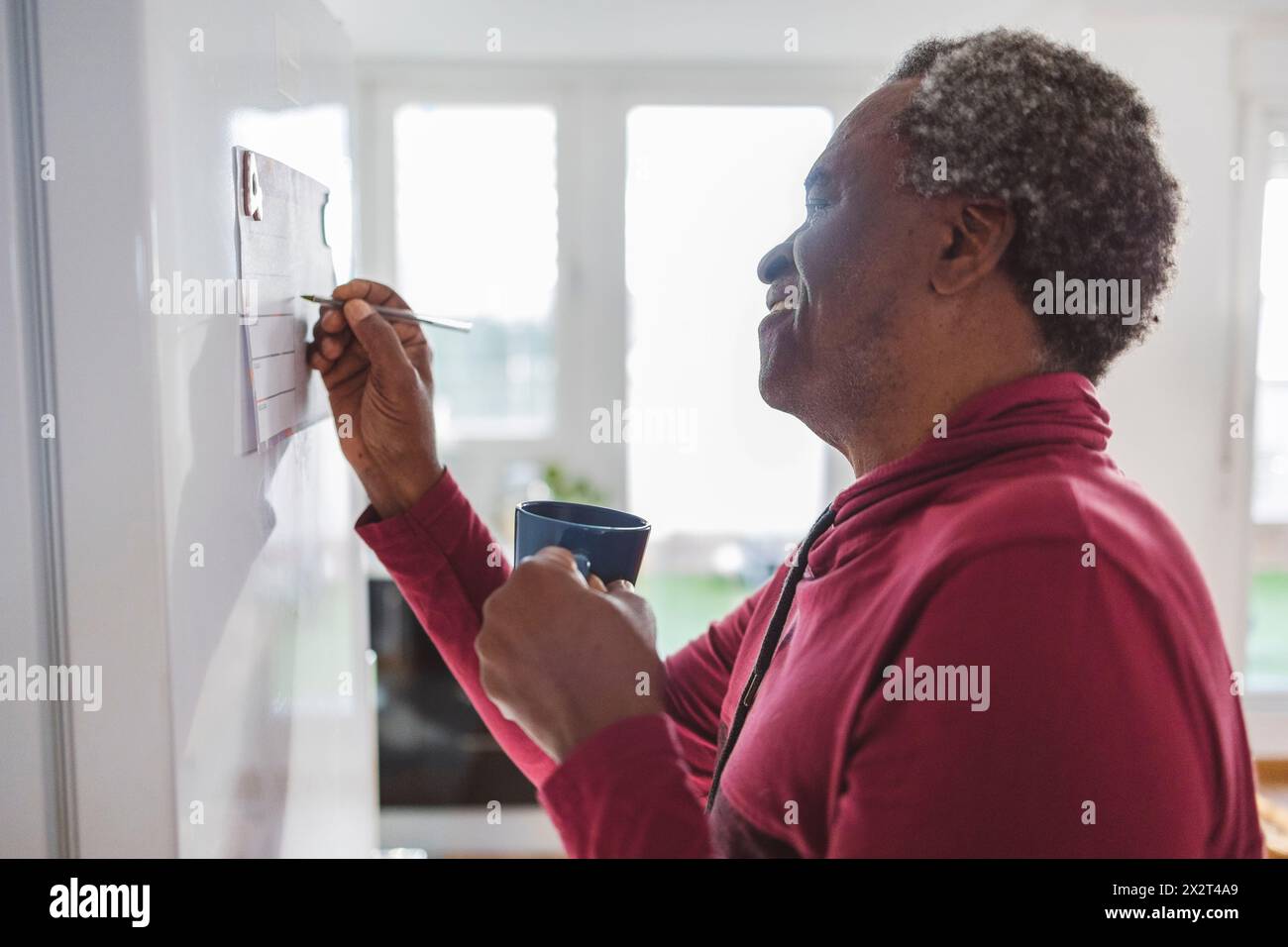 Homme senior souriant tenant la tâche d'écriture de tasse de thé sur le calendrier à la maison Banque D'Images