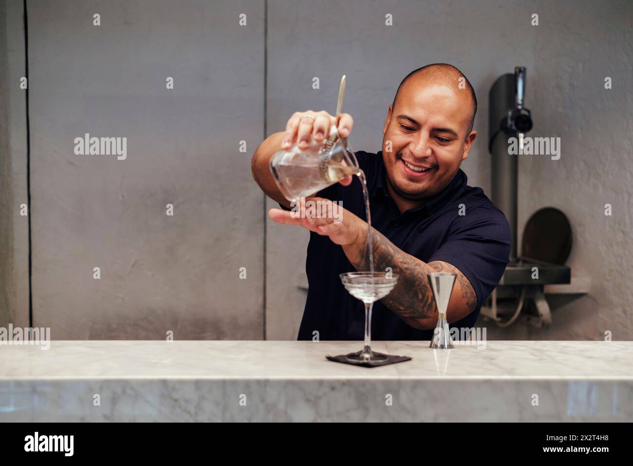 Barman souriant versant un cocktail dans un verre au comptoir du bar Banque D'Images