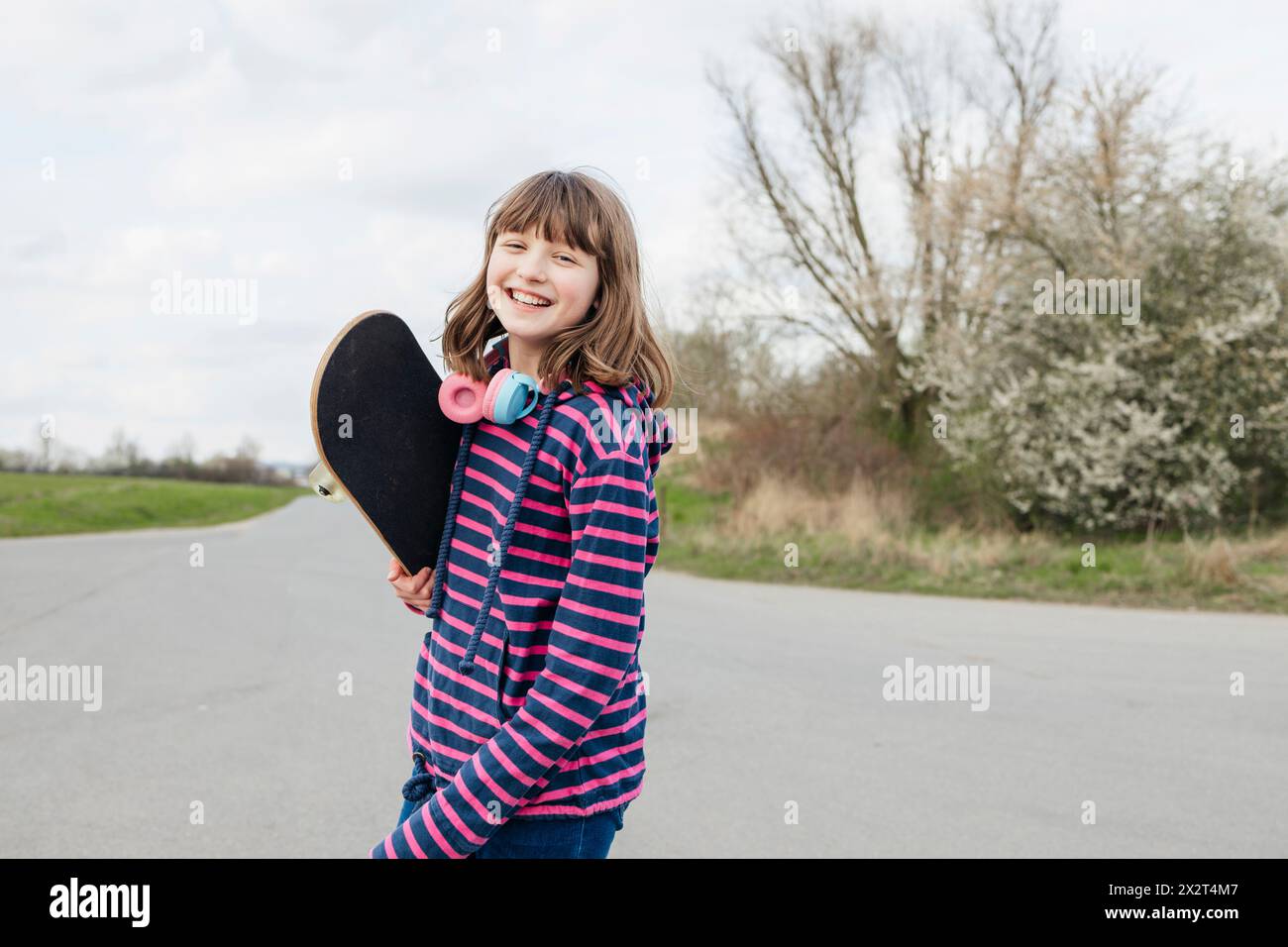 Fille heureuse debout avec skateboard sur la route Banque D'Images