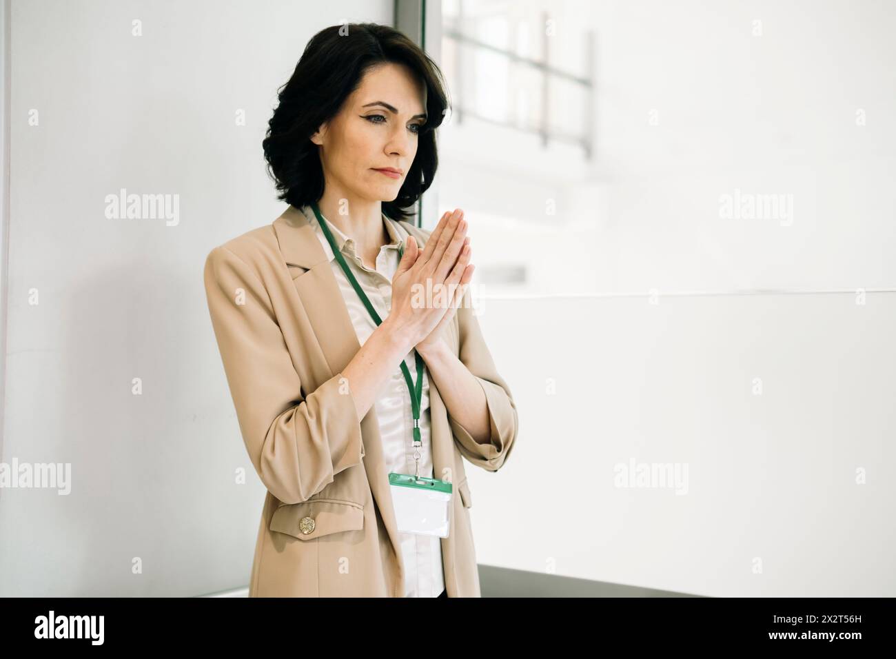 Femme d'affaires mature inquiète debout avec les mains serrées contemplant au bureau Banque D'Images