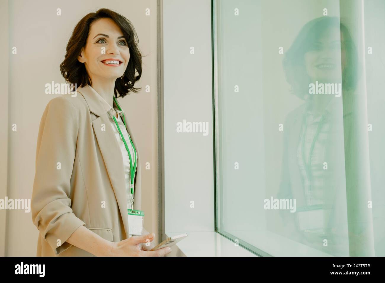 Femme d'affaires souriante regardant par la fenêtre au bureau Banque D'Images