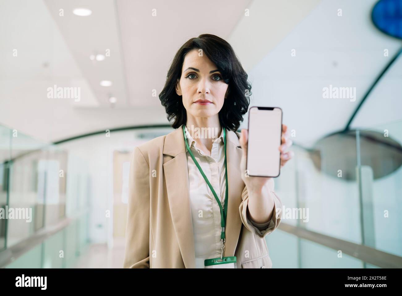 Femme d'affaires mature confiante montrant le téléphone intelligent avec l'écran blanc au bureau Banque D'Images