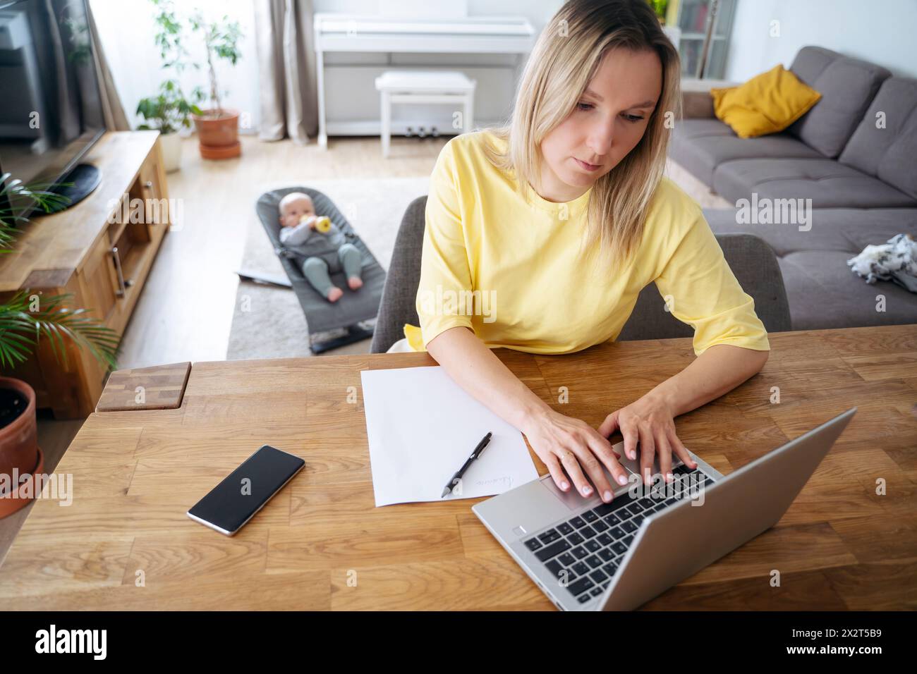 Femme d'affaires blonde utilisant un ordinateur portable à table avec son fils en arrière-plan Banque D'Images