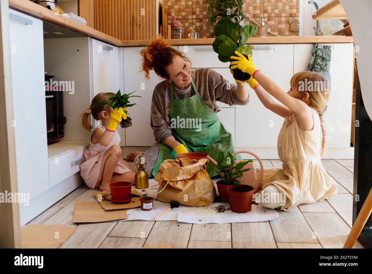 Mère et filles tenant des plantes en pot dans la cuisine à la maison Banque D'Images