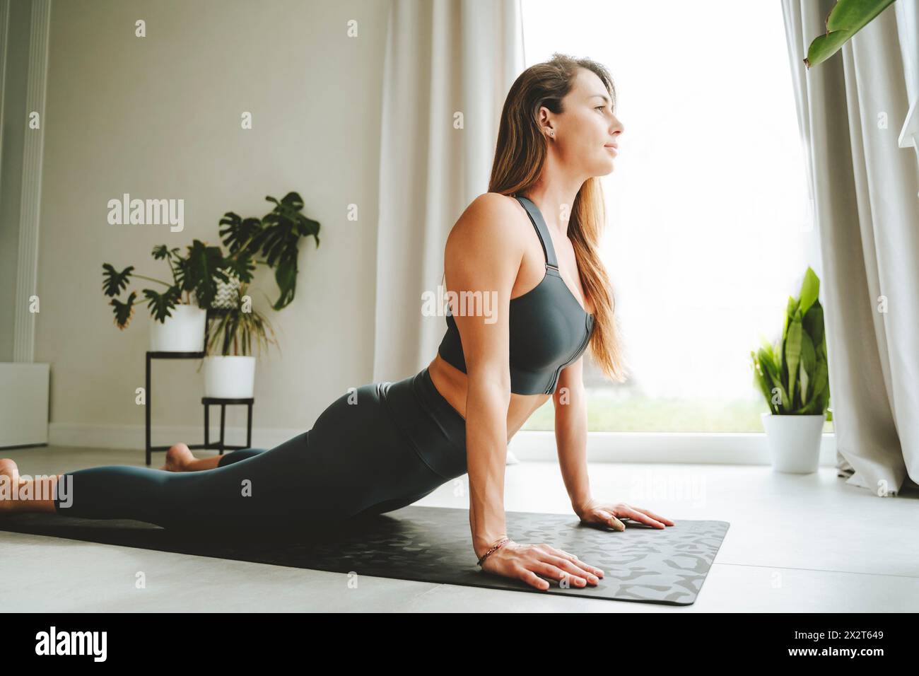 Femme pratiquant Cobra pose sur tapis de yoga à la maison Banque D'Images