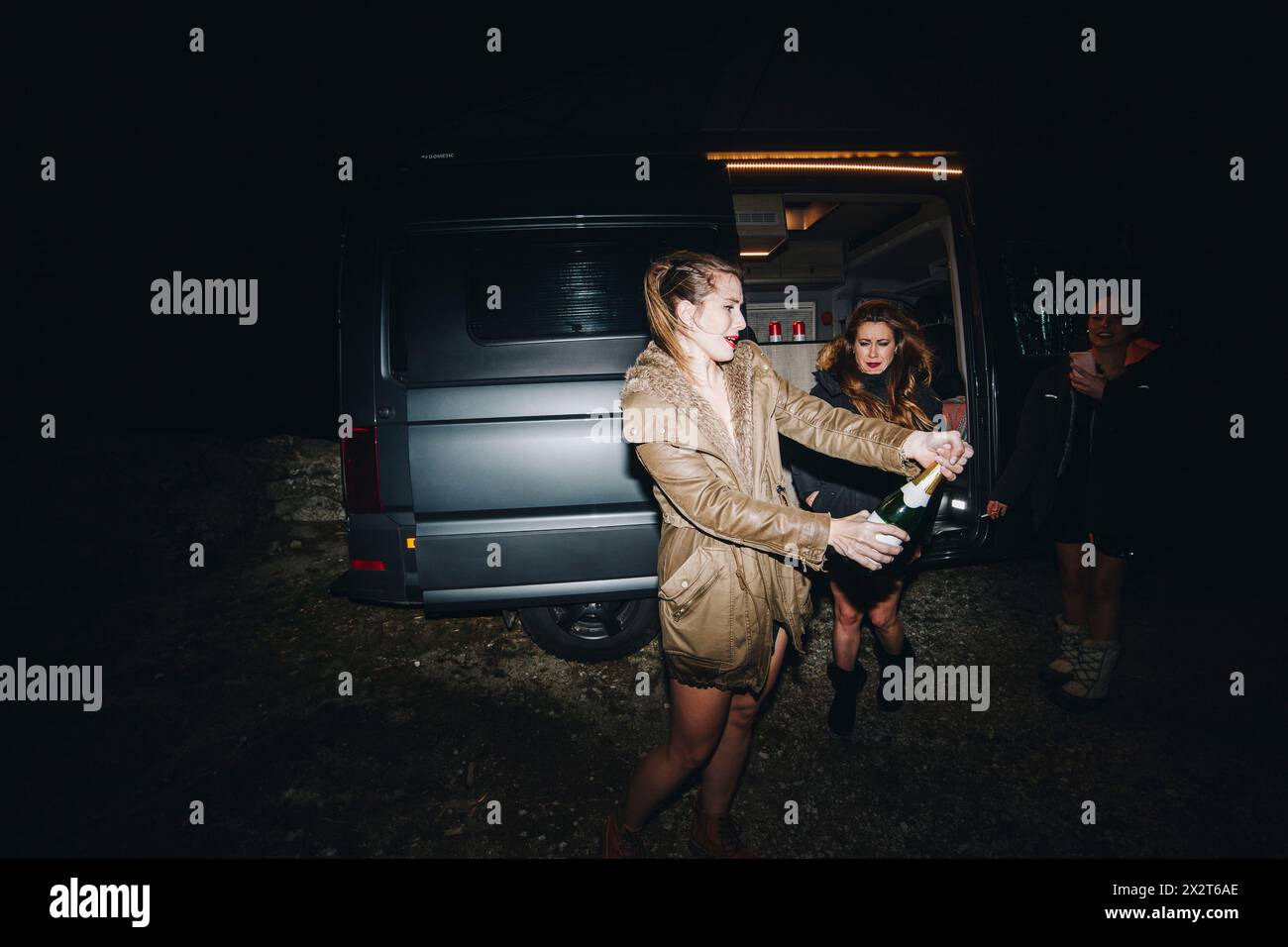 Femme ouvrant une bouteille de champagne célébrant le réveillon du nouvel an avec des amis près du camping-car la nuit Banque D'Images