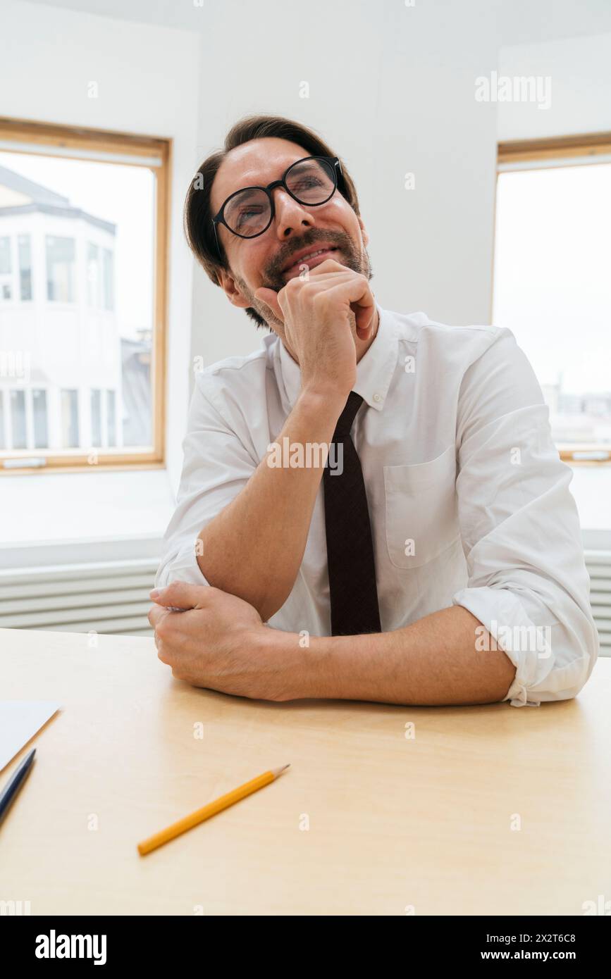 Homme d'affaires souriant et attentionné assis au bureau dans le bureau Banque D'Images