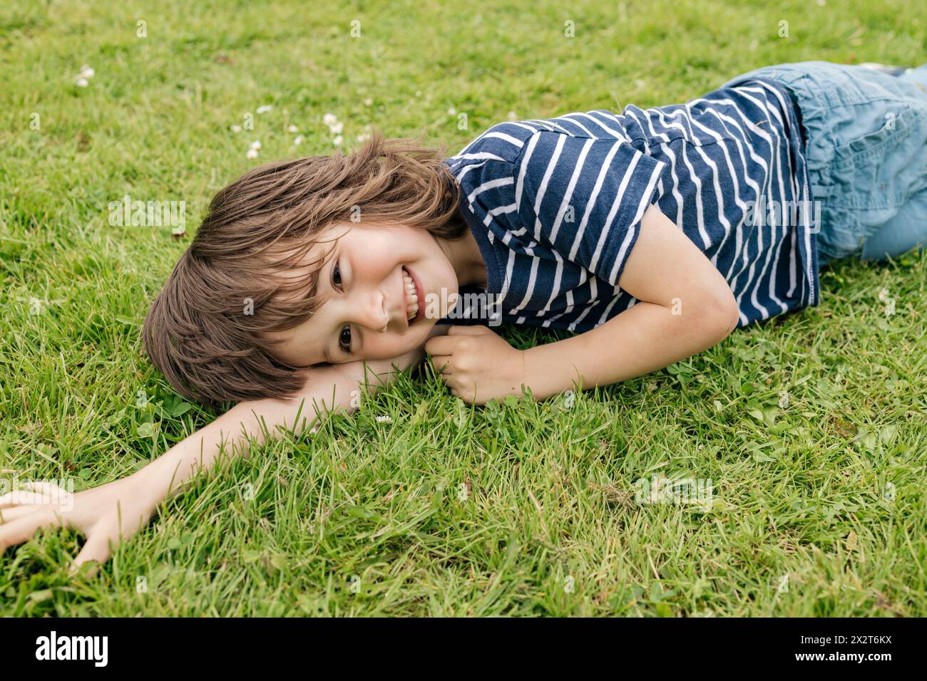 Garçon heureux en t-shirt rayé couché sur l'herbe dans la pelouse Banque D'Images