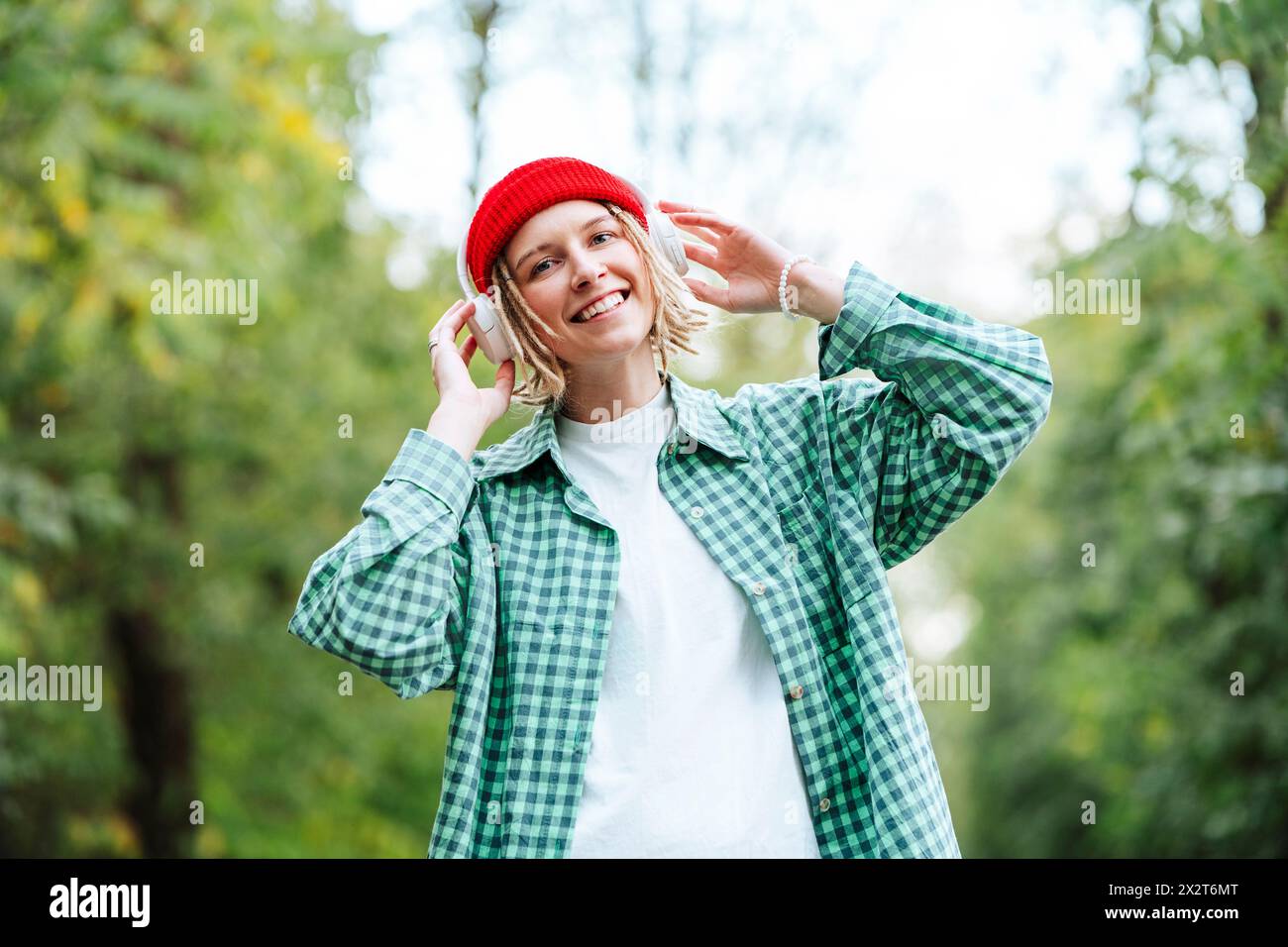 Femme heureuse portant un chapeau en tricot rouge et écoutant de la musique à travers des écouteurs sans fil Banque D'Images