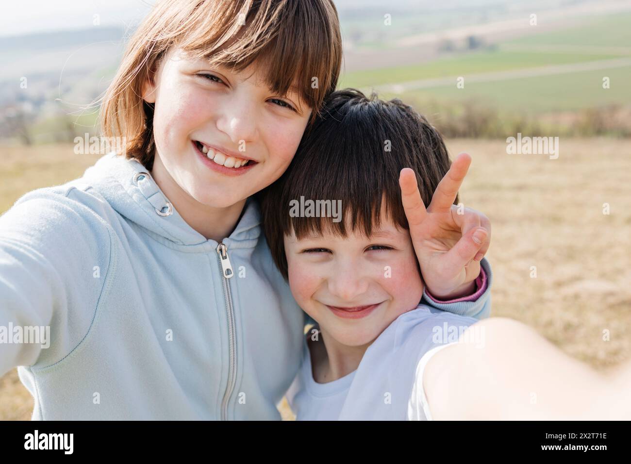 Fille souriante montrant le signe de paix et prenant selfie avec frère Banque D'Images