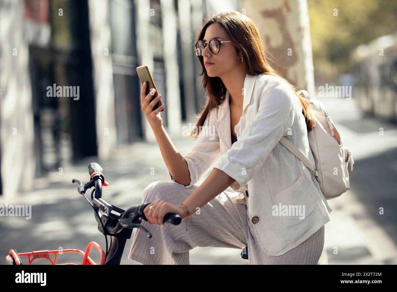 Jeune femme d'affaires sur le vélo en utilisant le téléphone intelligent à la rue Banque D'Images