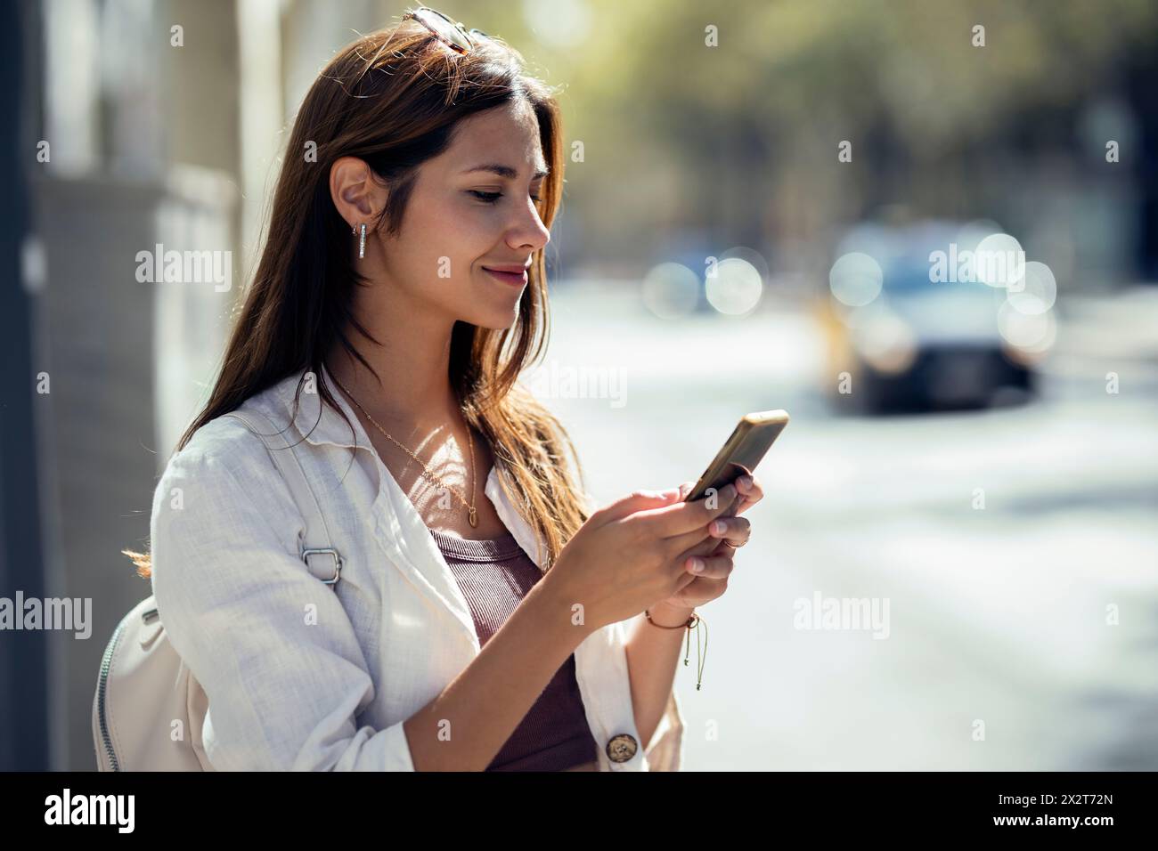 Femme d'affaires souriante utilisant un smartphone dans la rue Banque D'Images