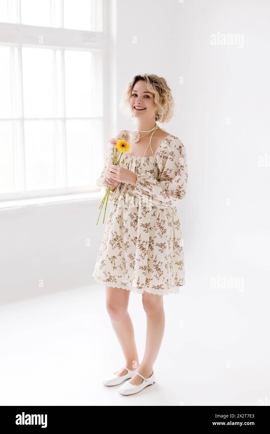 Femme blonde souriante debout avec des fleurs Banque D'Images