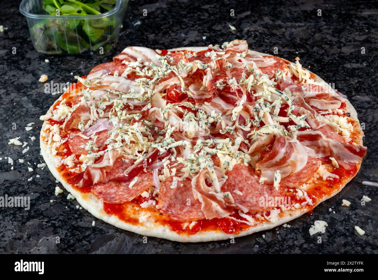 Voici une délicieuse pizza ornée de jambon, salami, fromage, oignons et herbes fraîches, reposant sur un comptoir de cuisine en granit, attendant impatiemment son tu Banque D'Images