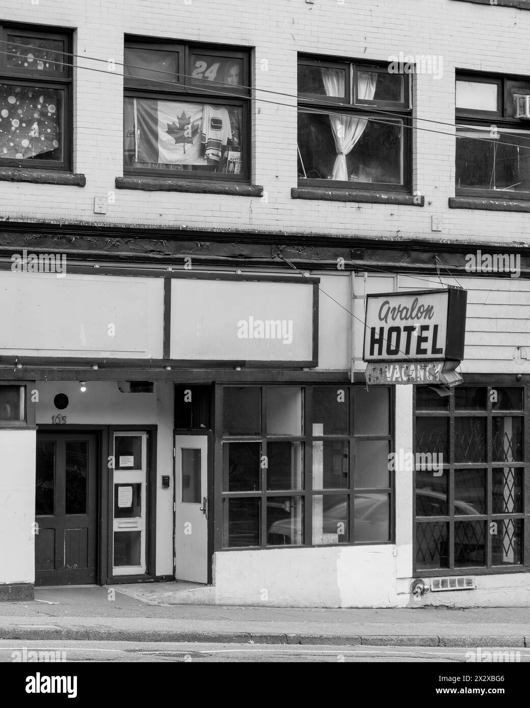 Une photo en noir et blanc d'un vieil hôtel sur la rue Pender avec son panneau de vacance battu et son mur patché, et des rideaux, drapeaux, affiches sur les fenêtres. Banque D'Images