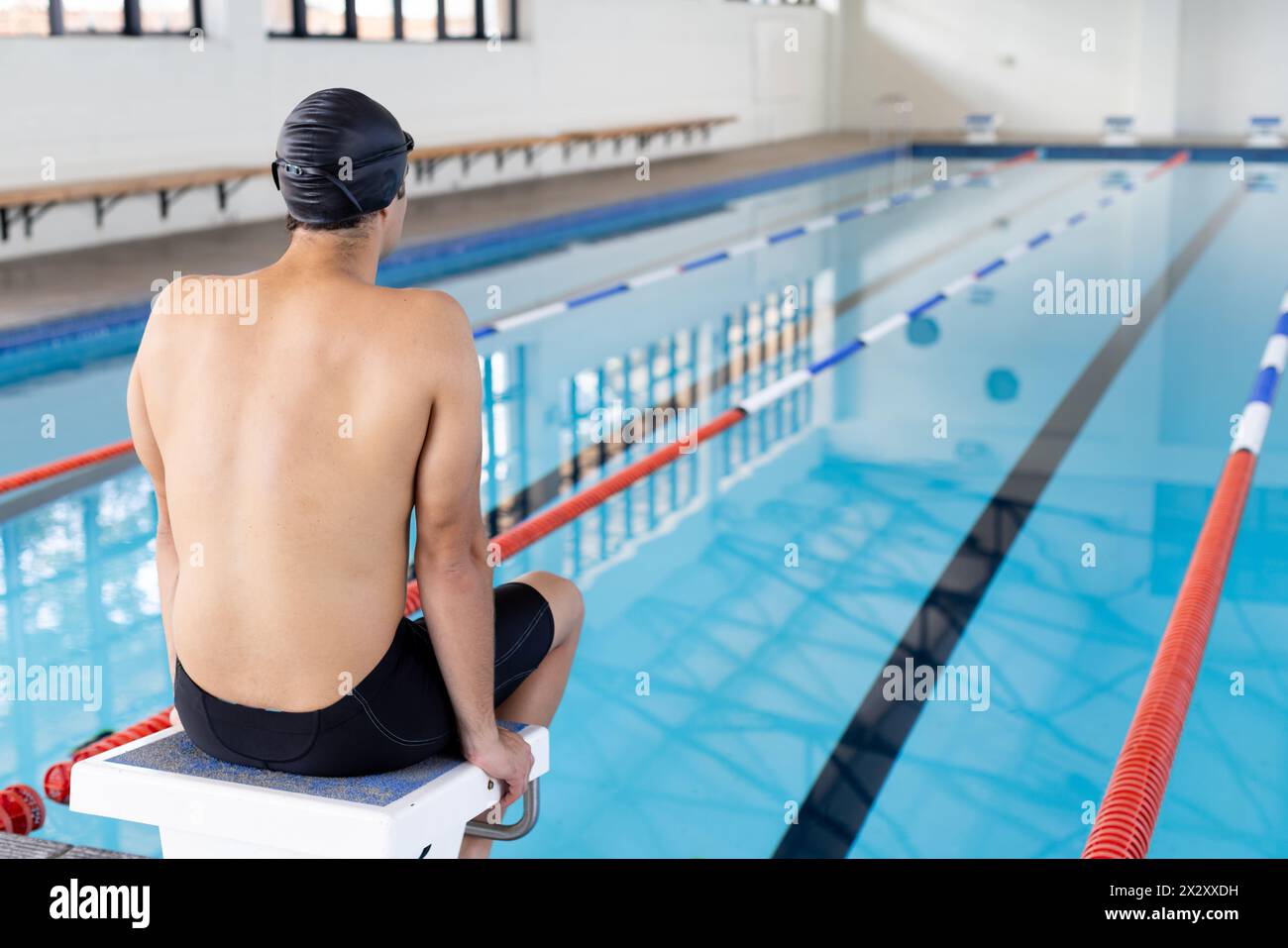 Jeune nageur masculin caucasien assis au bord de la piscine à l'intérieur, se préparant à plonger, copier l'espace Banque D'Images