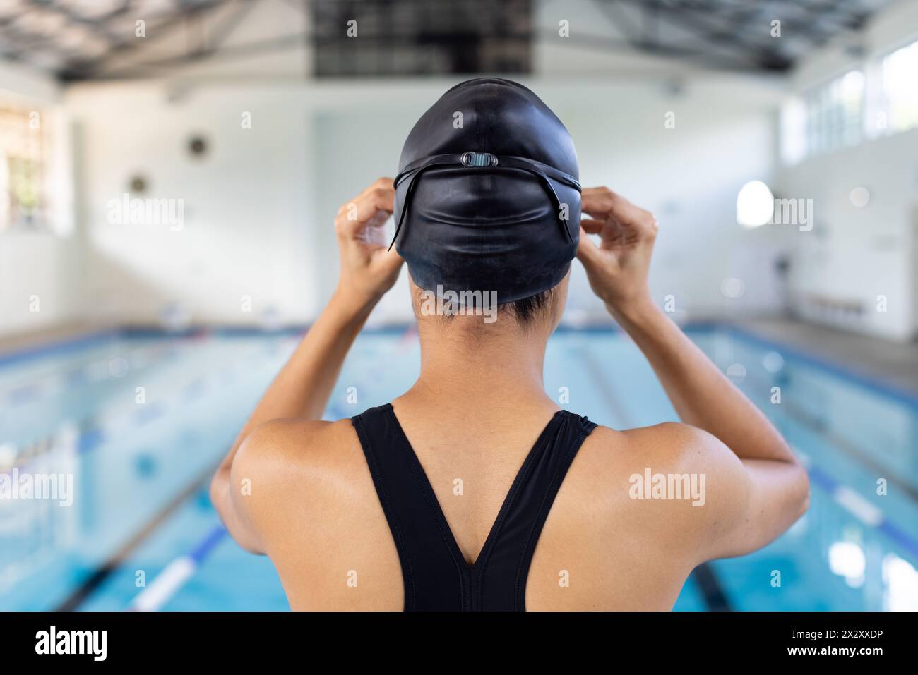 Biracial jeune femme nageuse ajustable bonnet de bain, debout au bord de la piscine à l'intérieur Banque D'Images