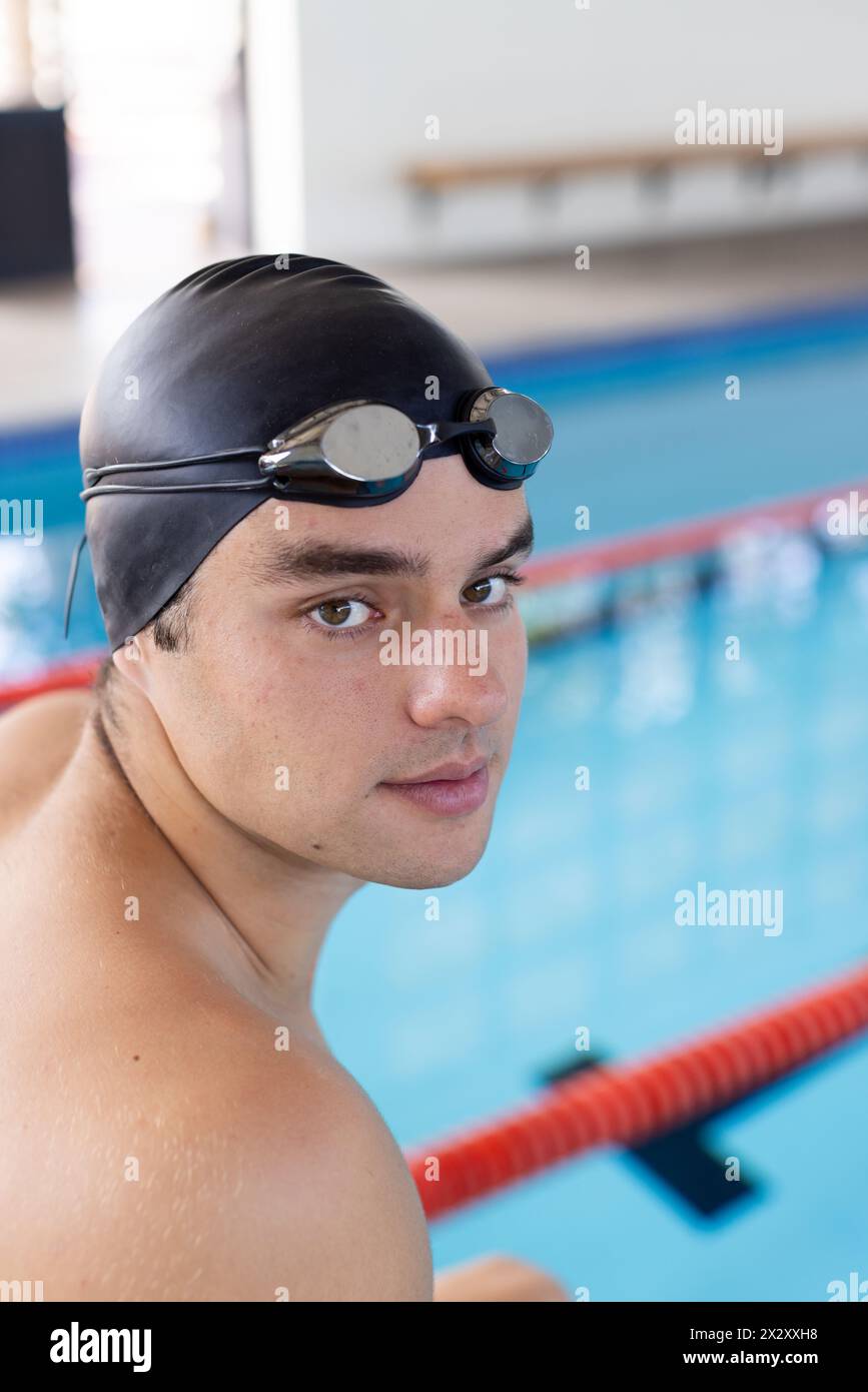 Jeune nageur caucasien debout près de la piscine à l'intérieur, regardant la caméra Banque D'Images