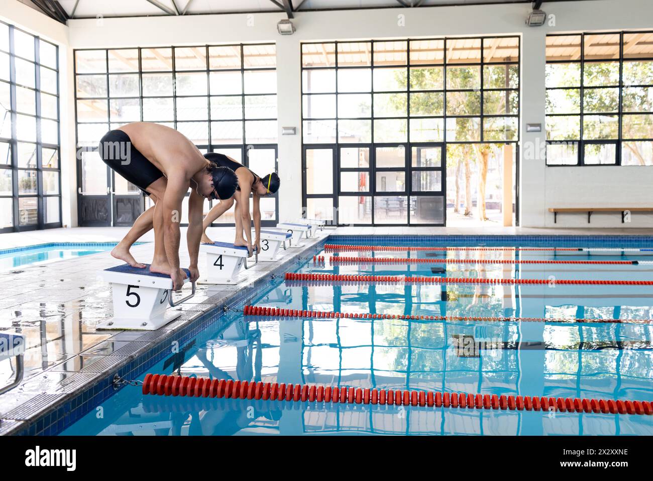 Divers jeunes compétiteurs nageurs, y compris un homme caucasien et une femme biraciale, se préparant à plonger Banque D'Images