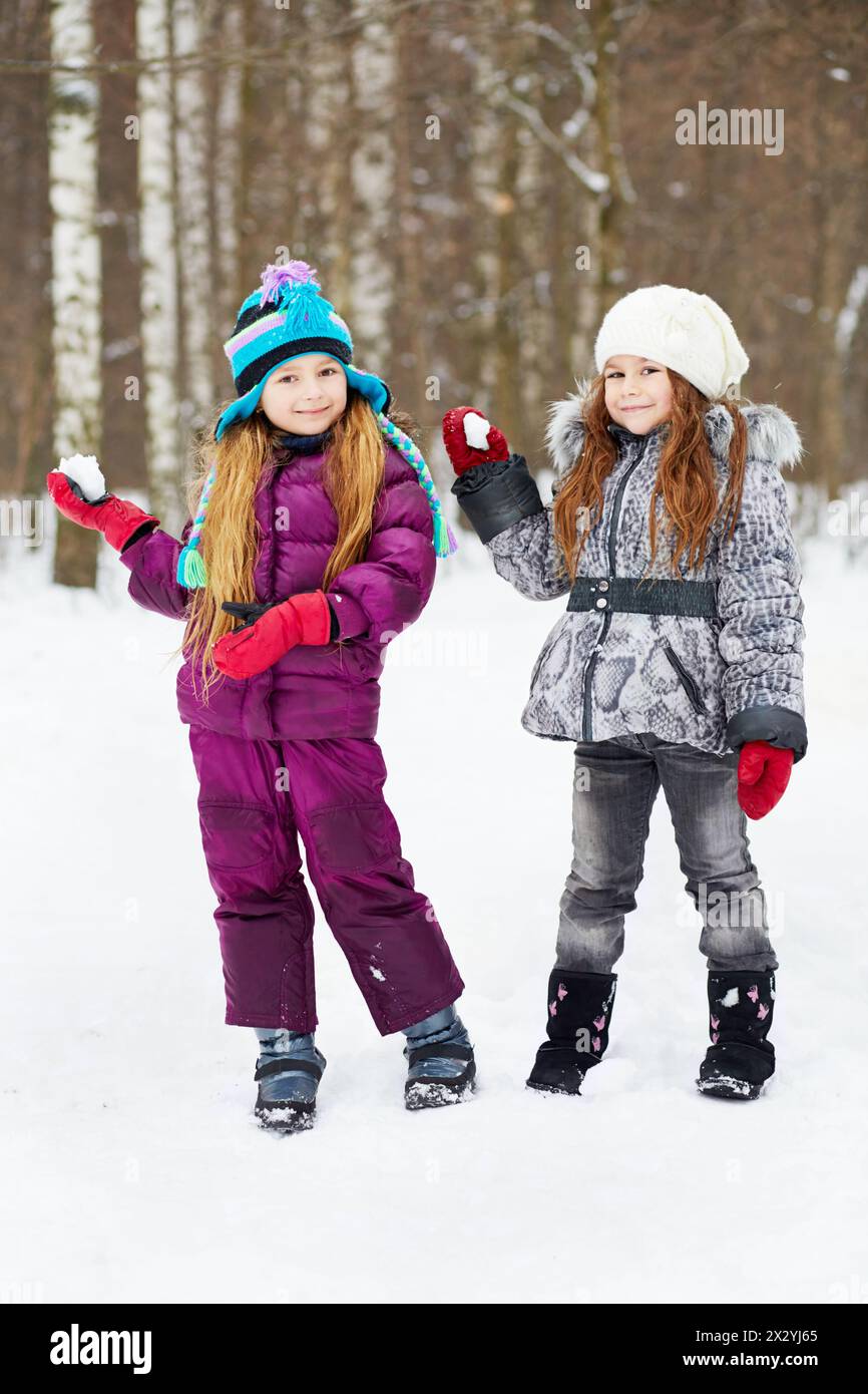 Deux copines souriantes se tiennent dans le parc d'hiver prêt à lancer des boules de neige Banque D'Images